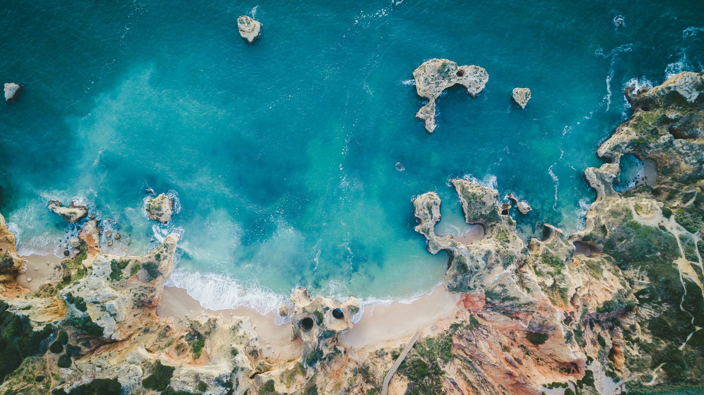 Vista aérea da costa rochosa do Algarve junto a Lagos, com falésias e água turquesa